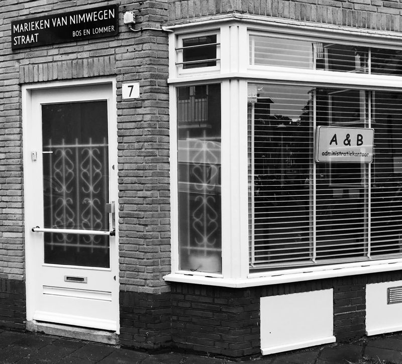 Het kantoor aan de Marieken van Nimwegenstraat: een witte voordeur en een erker met het bord &ldquo;A & B administratiekantoor&rdquo;, in zwart-wit.